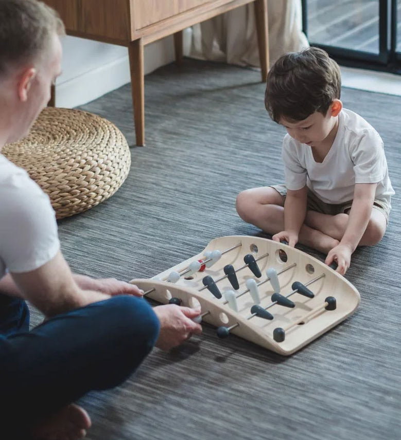 A child and adult playing with the PlanToys wooden soccer game. 