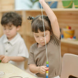 Child threading beads from the PlanToys threading beads wooden lacing toy set onto a long white lace.