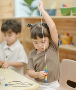 Child threading beads from the PlanToys threading beads wooden lacing toy set onto a long white lace.