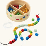 PlanToys threading beads wooden lacing toy. Rainbow coloured wooden beads threaded onto black and white laces, comes with a handy wooden storage box with compartments.