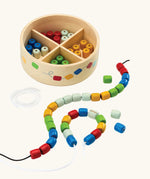 PlanToys threading beads wooden lacing toy. Rainbow coloured wooden beads threaded onto black and white laces, comes with a handy wooden storage box with compartments.