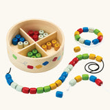 PlanToys threading beads wooden lacing toy. Rainbow coloured wooden beads with black and white laces in a handy wooden storage box with compartments.