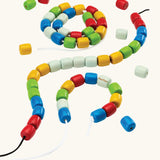 PlanToys threading beads wooden lacing toy. Rainbow coloured wooden beads threaded onto black and white laces.