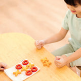 Child playing with the PlanToys Travel Tic-Tac-Toe wooden game set. Cotton bag printed with a grid with 5 yellow x pieces and 5 red o pieces.  