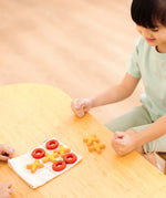 Child playing with the PlanToys Travel Tic-Tac-Toe wooden game set. Cotton bag printed with a grid with 5 yellow x pieces and 5 red o pieces.  
