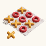 PlanToys Travel Tic-Tac-Toe wooden game set. Cotton storage bag printed with a grid with 5 yellow x pieces and 5 red o pieces.  