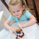 A child playing with the PlanToys Timber Tumble Game on white table. 