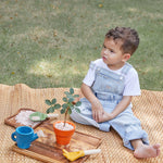 A child sitting on a mat outdoors playing with the A child playing with the PlanToys Gardening Set.