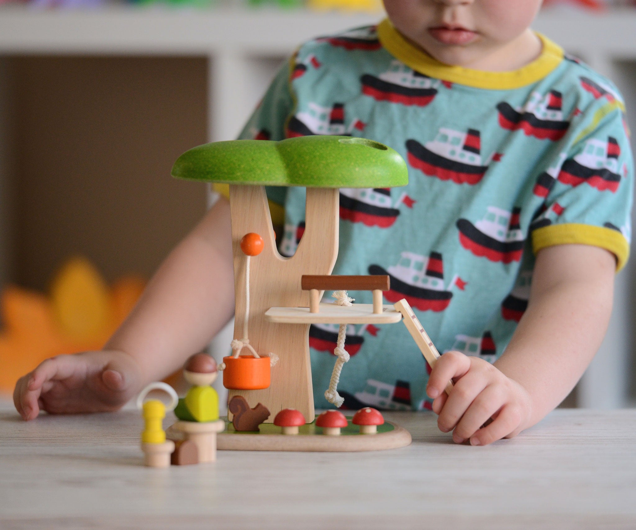 The PlanToys PlanWorld Tree House being played with by a child. The child's hand can be seen holding onto the little wooden ladder. 