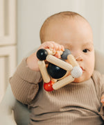 A baby clutching onto the PlanToys high contrast Triangle baby Clutching Toy. A black and natural wood wooden ball in a stretchy triangle clutching toy. PlanToys range of toys are made from sustainably sourced rubberwood, we're proud stockists of PlanToys here at Babipur. 