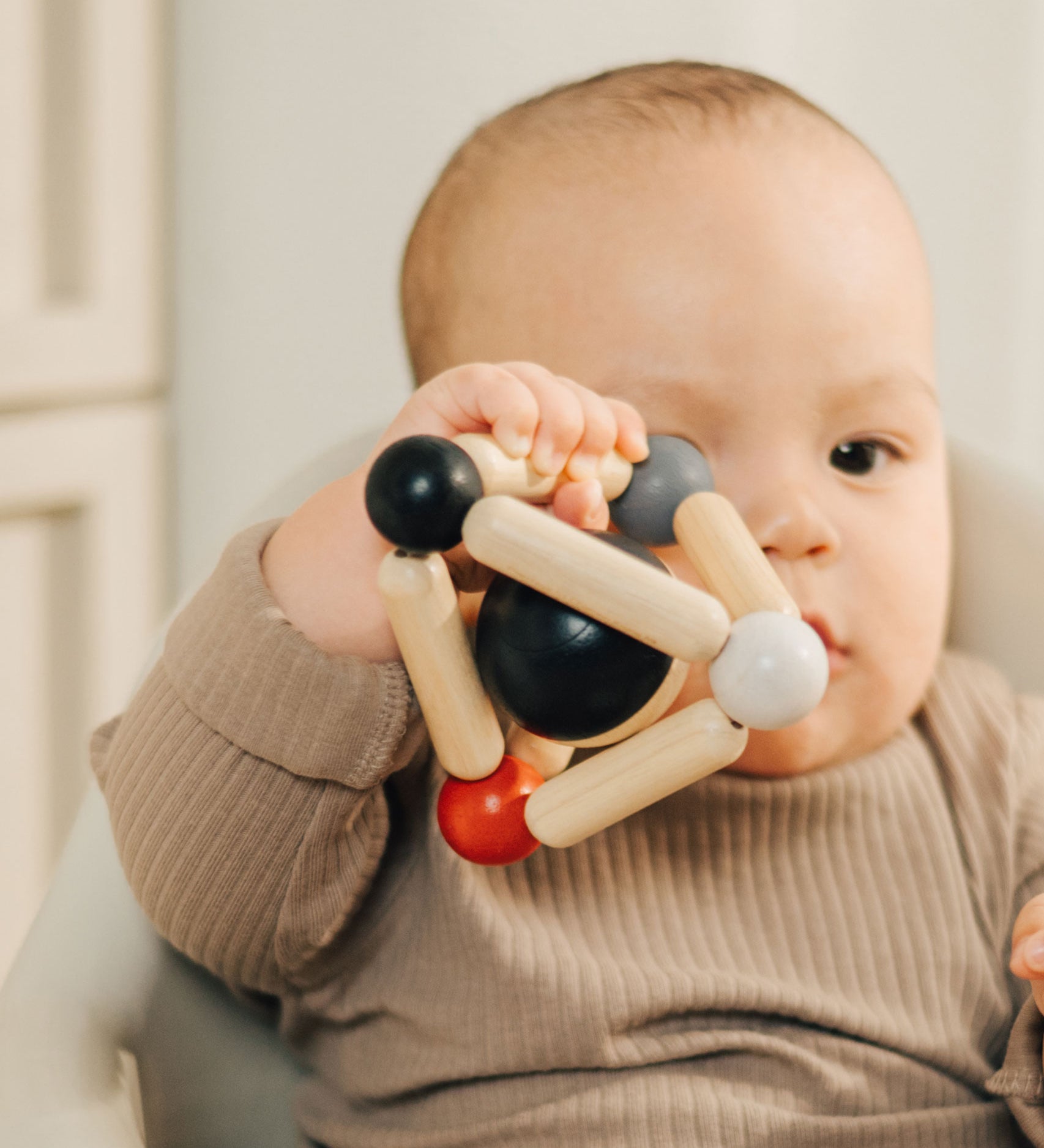 A baby clutching onto the PlanToys high contrast Triangle baby Clutching Toy. A black and natural wood wooden ball in a stretchy triangle clutching toy. PlanToys range of toys are made from sustainably sourced rubberwood, we're proud stockists of PlanToys here at Babipur. 