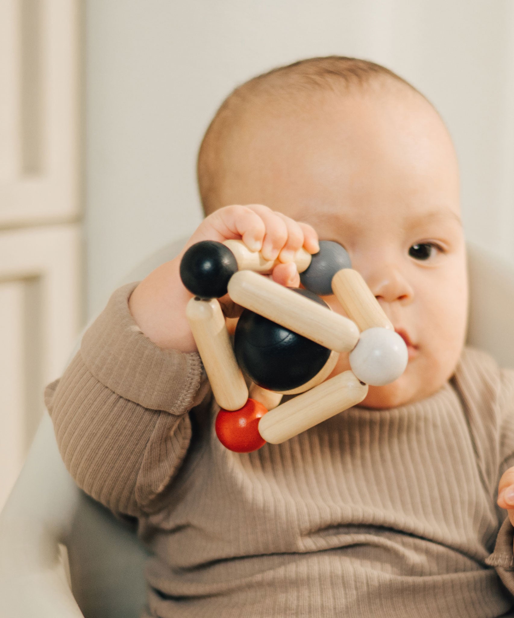 A baby clutching onto the PlanToys high contrast Triangle baby Clutching Toy. A black and natural wood wooden ball in a stretchy triangle clutching toy. PlanToys range of toys are made from sustainably sourced rubberwood, we're proud stockists of PlanToys here at Babipur. 