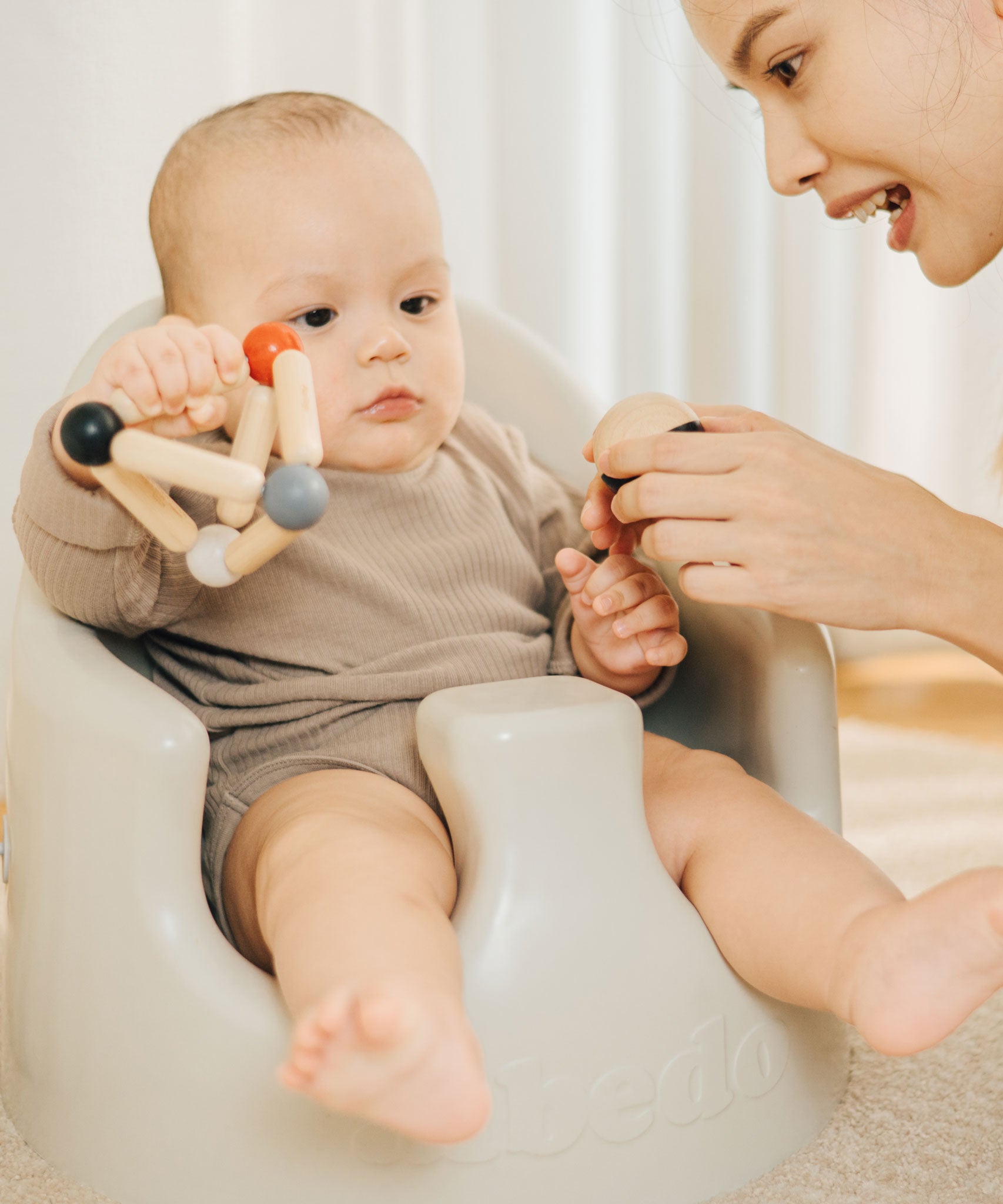 A baby playing with the PlanToys high contrast Triangle baby Clutching Toy. A black and natural wood wooden ball in a stretchy triangle clutching toy. PlanToys range of toys are made from sustainably sourced rubberwood, we're proud stockists of PlanToys here at Babipur. 