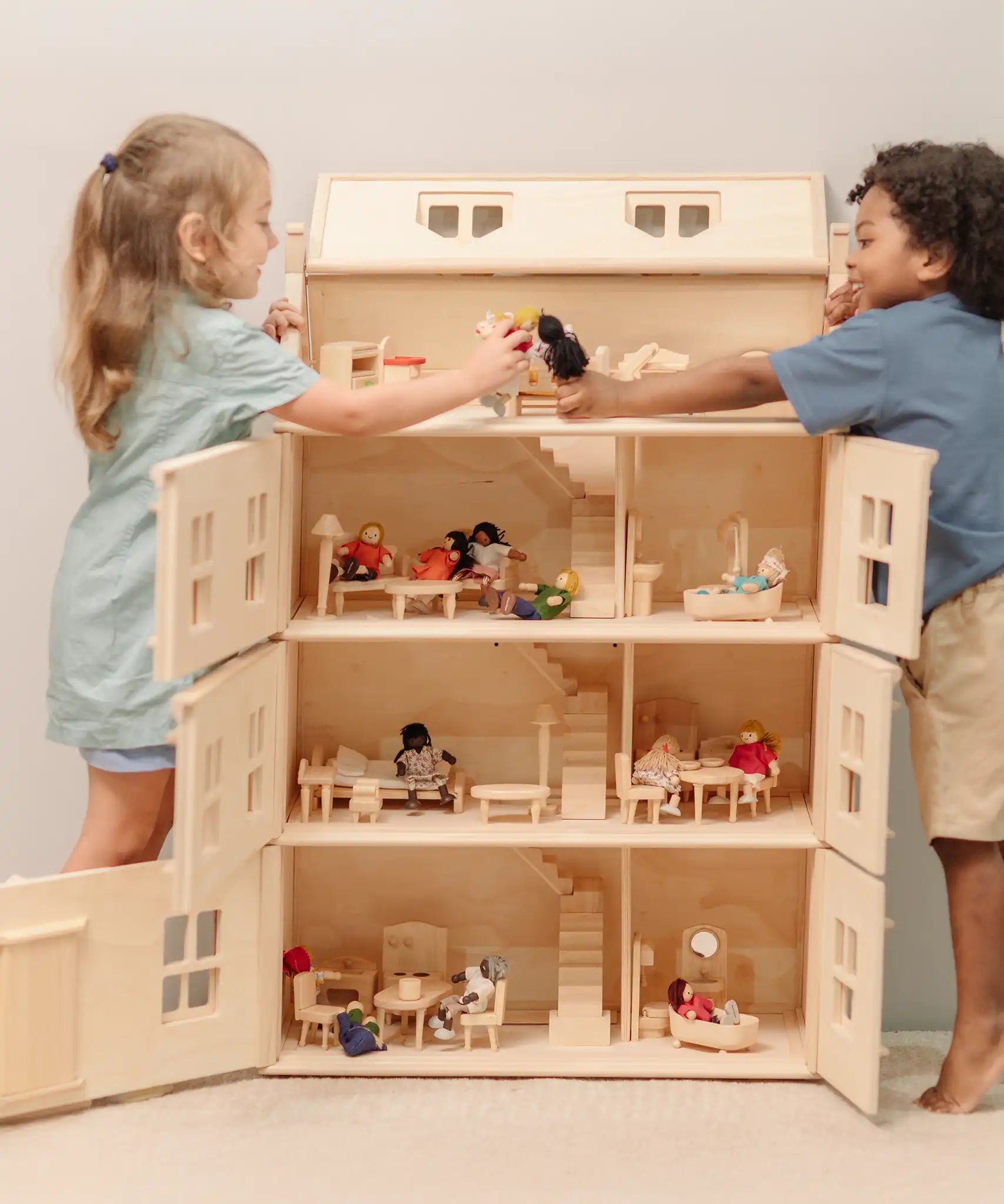 Children playing with the PlanToys Grand Victorian Dollhouse. Front and roof shown open and all floors and attic room has PlanToys dolls house furniture inside.