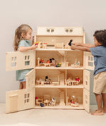 Children playing with the PlanToys Grand Victorian Dollhouse. Front and roof shown open and all floors and attic room has PlanToys dolls house furniture inside.