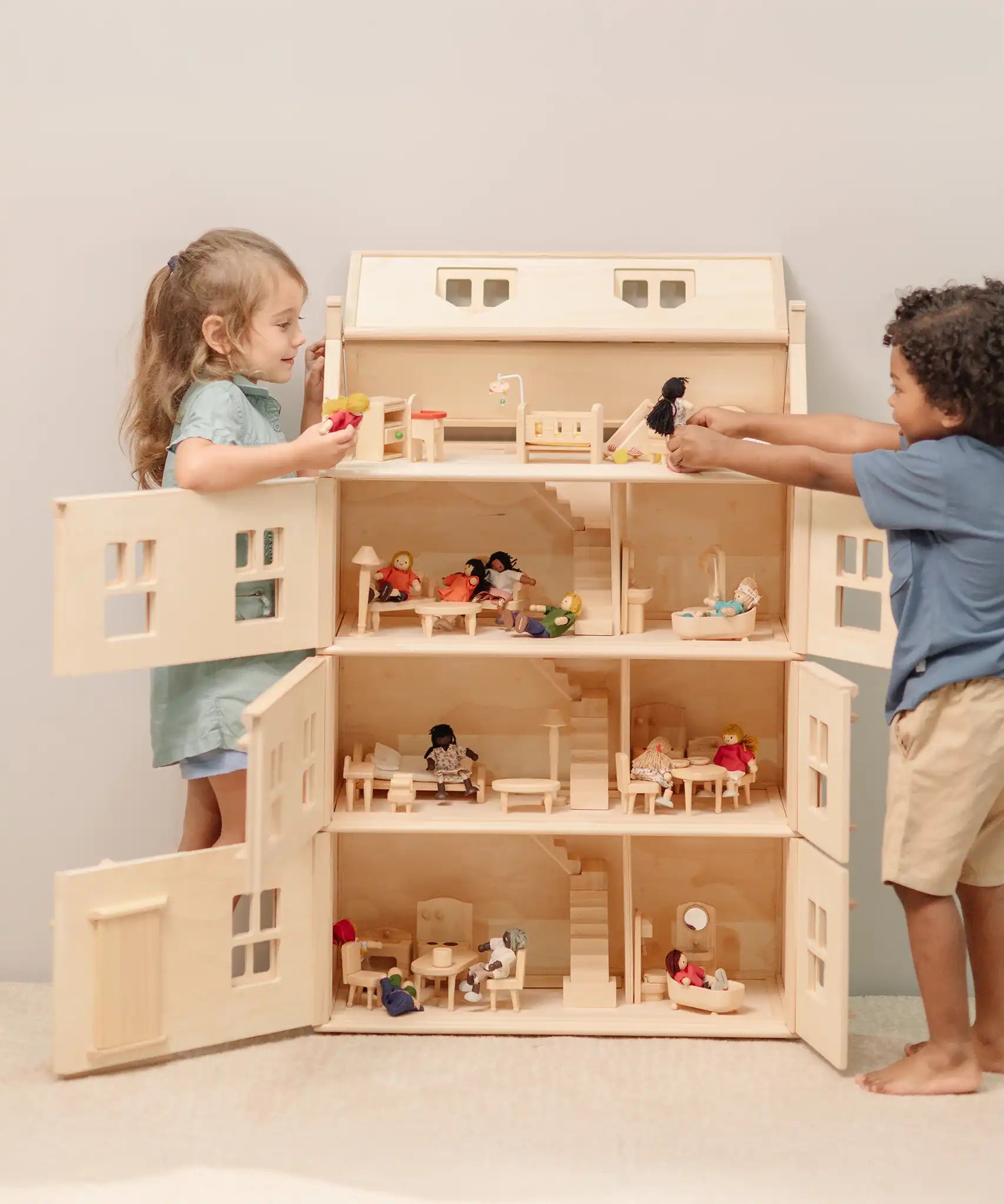 Children playing with the PlanToys Grand Victorian Dollhouse. Front and roof shown open and all floors and attic room has PlanToys dolls house furniture inside.