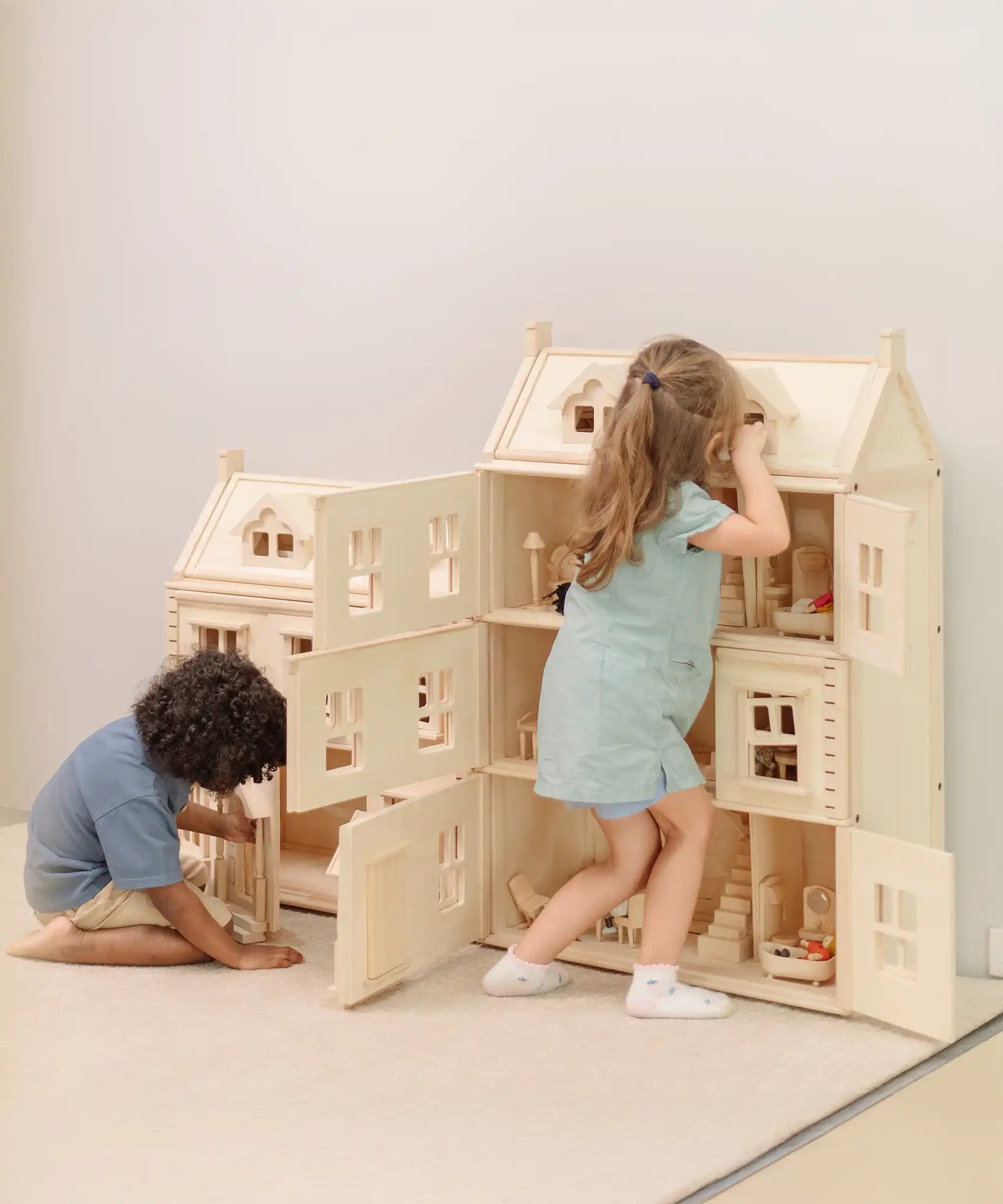 Children playing with the PlanToys Grand Victorian Dollhouse. The smaller Victorian dolls house is next to it.