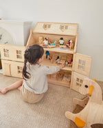 Girl sat on the floor next to the PlanToys Victorian dollhouse