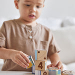Young boy ordering the numbers on the back of the PlanToys plastic-free animal puzzle blocks on a beige sofa