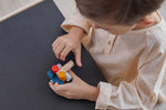 Close up of young child slotting together pieces from the PlanToys wooden logs puzzle on a black table