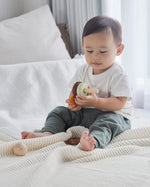 Young boy sat on a white bed playing with the PlanToys wooden stacking rings Waldorf toy