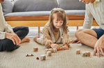 Young girl laying on the floor playing with the small wooden dog figure from the PlanToys plastic-free storytelling dice set