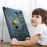 A child laying in front of a the PlanToys Wall Ball Game. The child has decorated the board with drawings. 

