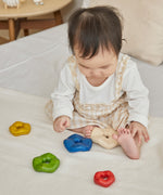 A baby playing with the Plan Toys wooden Wave Stacker - a tactile stacking rainbow baby toy.