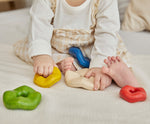 A close up of a child's hands playing with the Plan Toys Wave Stacker - a wooden stacking baby toy in rainbow colours.