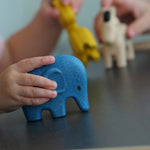 A child playing with the PlanToys Wild Animals Set, a child's hand can be seen holding the blue coloured elephant figure with the other animal figures in the background,