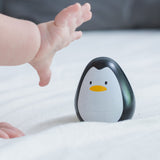 A baby's hand reaching for the PlanToys wobbly wooden penguin toy. 