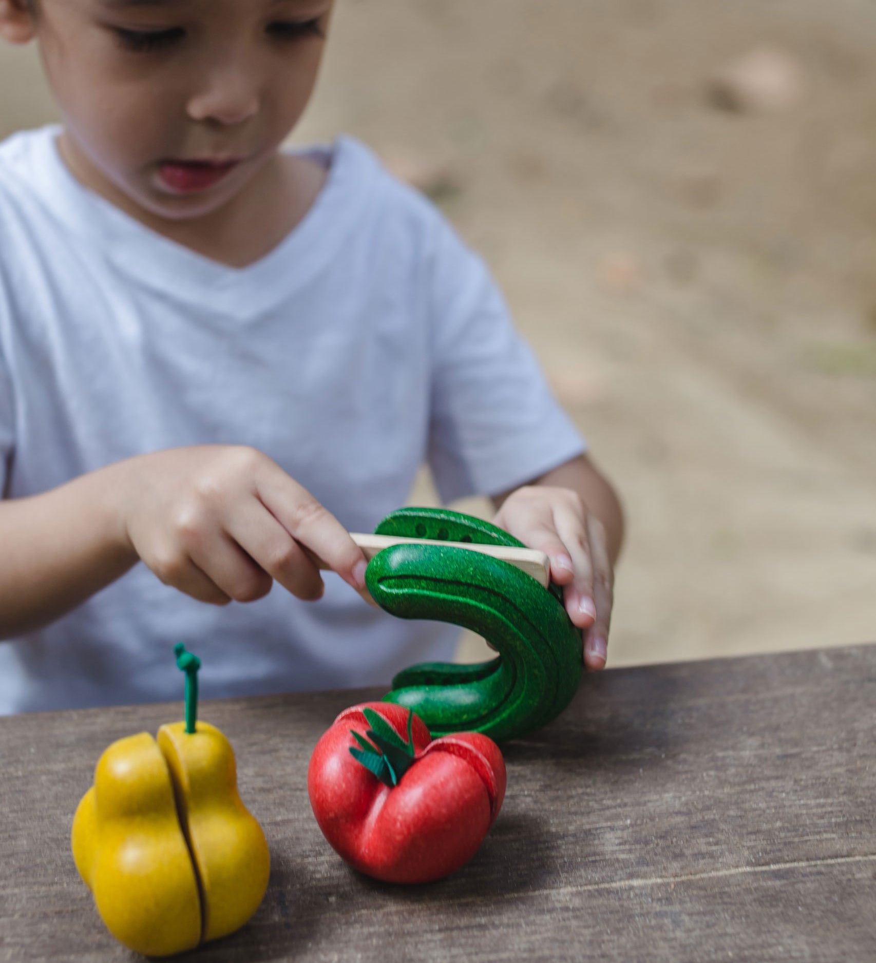 A child cutting up the toy cucumber from the PlanToys Wonky Fruit & Vegetables set. 