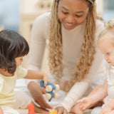 Two children and an adult playing with the PlanToys Dino wooden Car toys. A blue coloured diplodocus, a yellow stegosaurus and red coloured t-rex dinosaur figures on wheels. PlanToys range of toys are made from sustainably sourced rubberwood, we're proud stockists of PlanToys here at Babipur. 