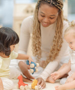 Two children and an adult playing with the PlanToys Dino wooden Car toys. A blue coloured diplodocus, a yellow stegosaurus and red coloured t-rex dinosaur figures on wheels. PlanToys range of toys are made from sustainably sourced rubberwood, we're proud stockists of PlanToys here at Babipur. 