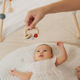 A close up of an adult's hand holding up a PlanToys Beads Rattle in a High Contrast colourway above a baby. 
PlanToys range of toys are made from sustainably sourced rubberwood, we're proud stockists of PlanToys here at Babipur. 