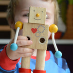 A close up of a child holding up a PlanToys Build a Robot toy. The robot has it's square shaped face on with a happy expression. 