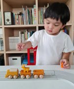 Child playing with the PlanToys yellow wooden cargo train on a rubber railway track set and small wooden animal figures. 