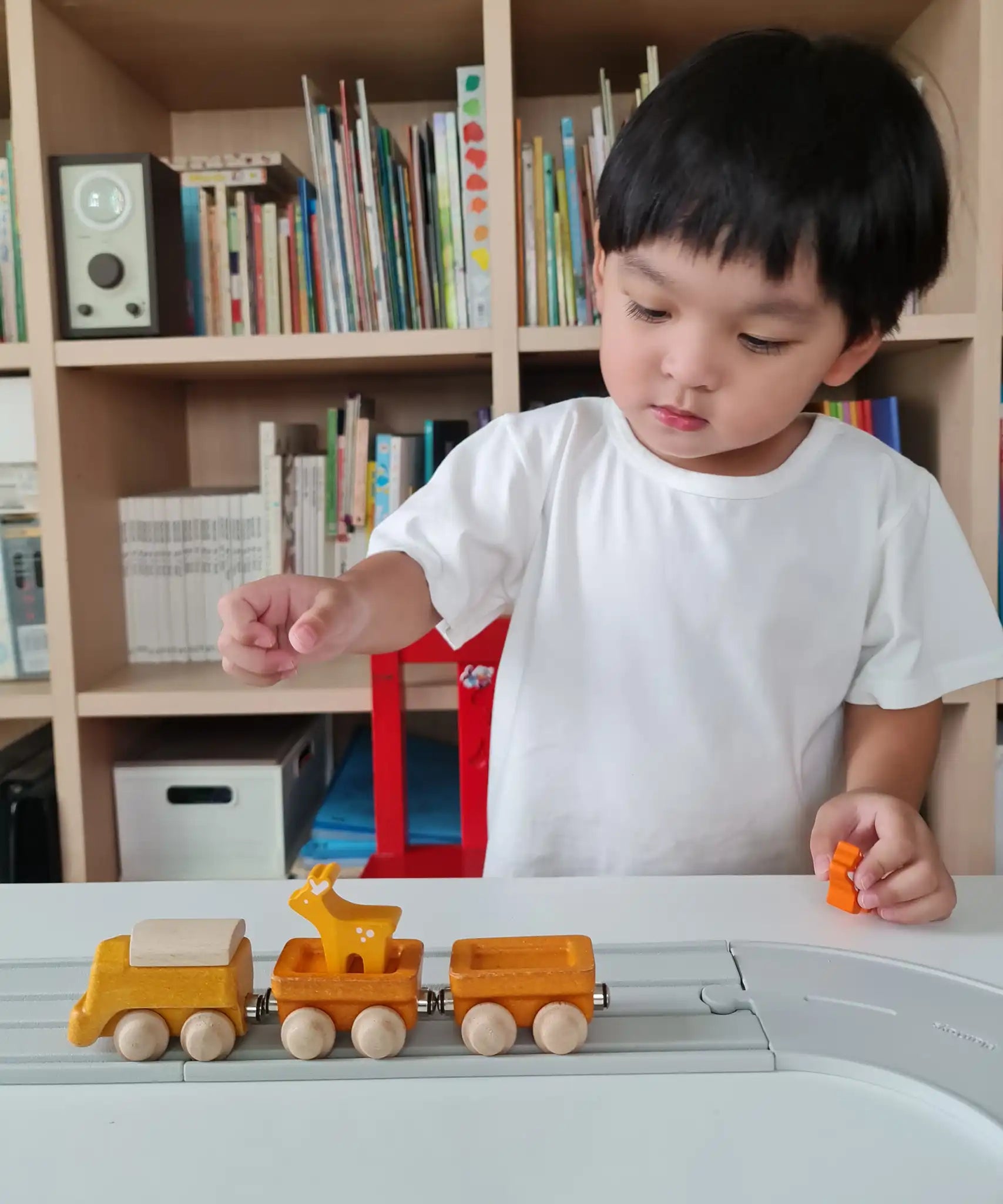 Child playing with the PlanToys yellow wooden cargo train on a rubber railway track set and small wooden animal figures. 
