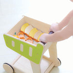A PlanToys Shopping Trolley on a white surface, a child's hand can be seen pushing the trolley along. 