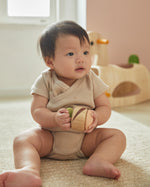Young child sat on the floor holding the PlanToys plastic-free wooden sensory clapping roller toy. 
