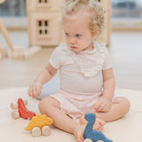 A child playing with the PlanToys Dino wooden Car toys. A blue coloured diplodocus, a yellow stegosaurus and red coloured t-rex dinosaur figures on wheels. PlanToys range of toys are made from sustainably sourced rubberwood, we're proud stockists of PlanToys here at Babipur. 