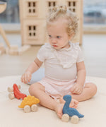 A child playing with the PlanToys Dino wooden Car toys. A blue coloured diplodocus, a yellow stegosaurus and red coloured t-rex dinosaur figures on wheels. PlanToys range of toys are made from sustainably sourced rubberwood, we're proud stockists of PlanToys here at Babipur. 