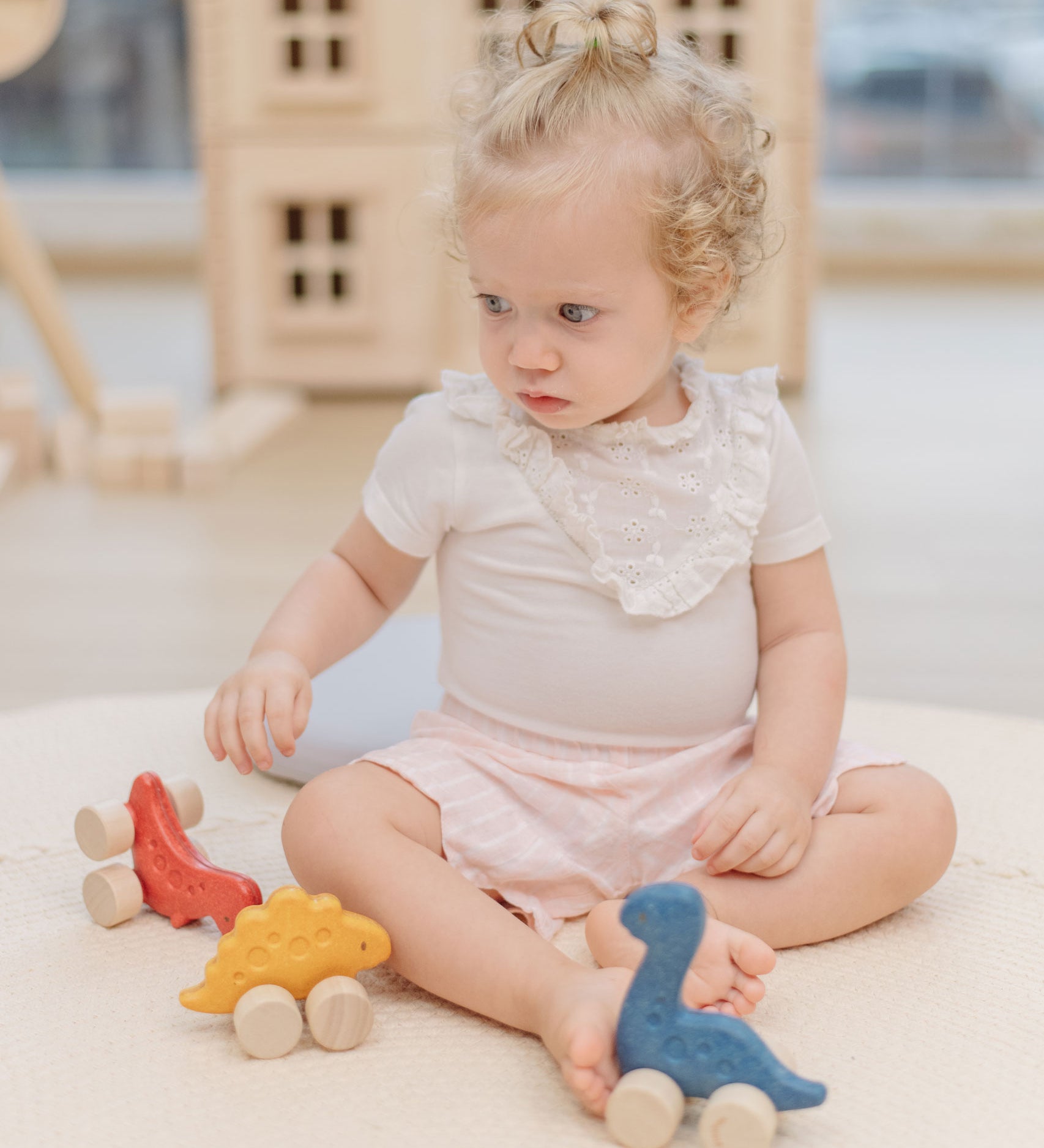 A child playing with the PlanToys Dino wooden Car toys. A blue coloured diplodocus, a yellow stegosaurus and red coloured t-rex dinosaur figures on wheels. PlanToys range of toys are made from sustainably sourced rubberwood, we're proud stockists of PlanToys here at Babipur. 