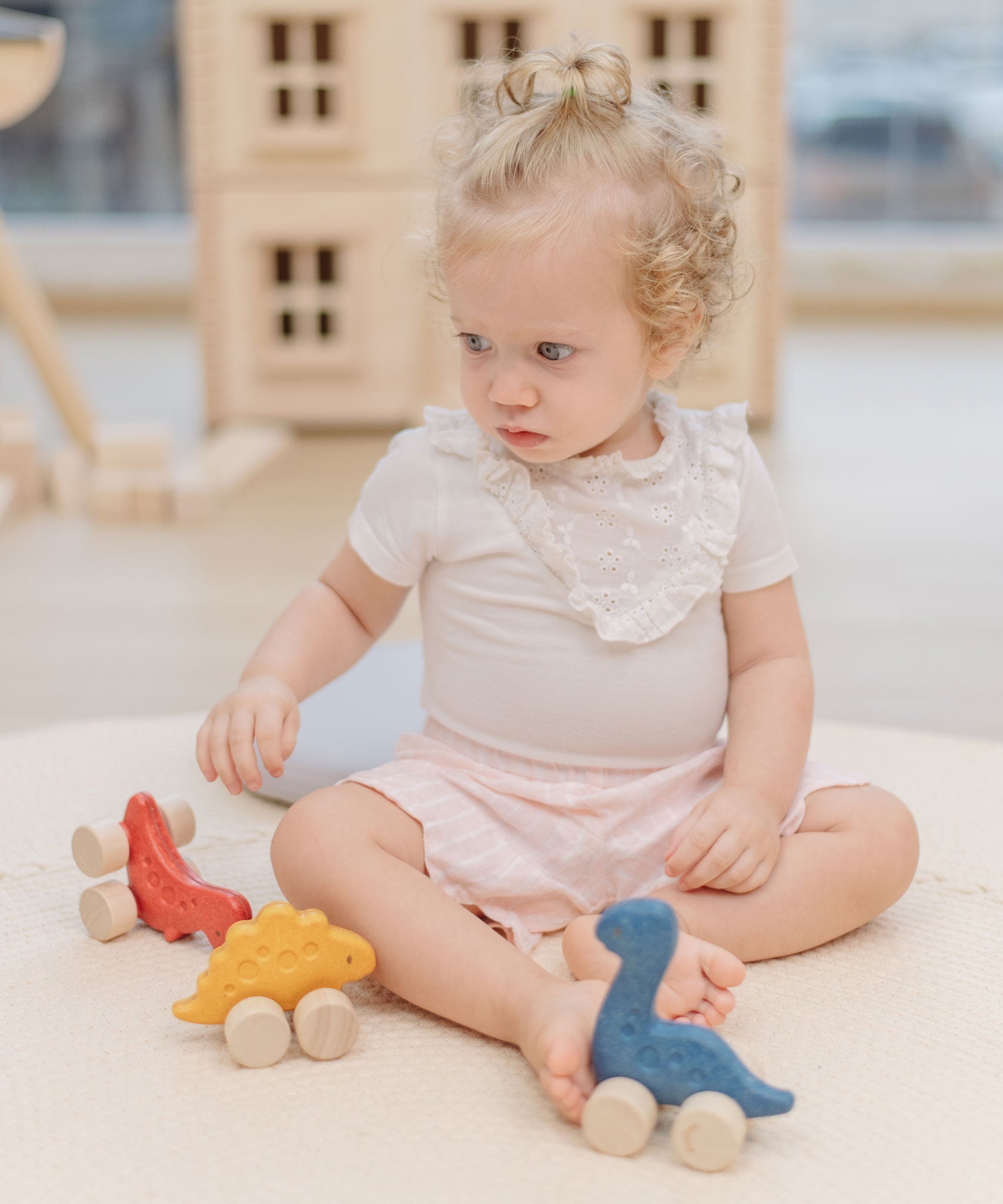 A child playing with the PlanToys Dino wooden Car toys. A blue coloured diplodocus, a yellow stegosaurus and red coloured t-rex dinosaur figures on wheels. PlanToys range of toys are made from sustainably sourced rubberwood, we're proud stockists of PlanToys here at Babipur. 