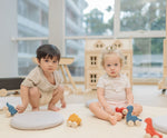 Two children playing with the PlanToys Dino wooden Car toys. A blue coloured diplodocus, a yellow stegosaurus and red coloured t-rex dinosaur figures on wheels. PlanToys range of toys are made from sustainably sourced rubberwood, we're proud stockists of PlanToys here at Babipur. 