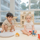 Two children playing with the PlanToys Dino wooden Car toys. A blue coloured diplodocus, a yellow stegosaurus and red coloured t-rex dinosaur figures on wheels. PlanToys range of toys are made from sustainably sourced rubberwood, we're proud stockists of PlanToys here at Babipur. 