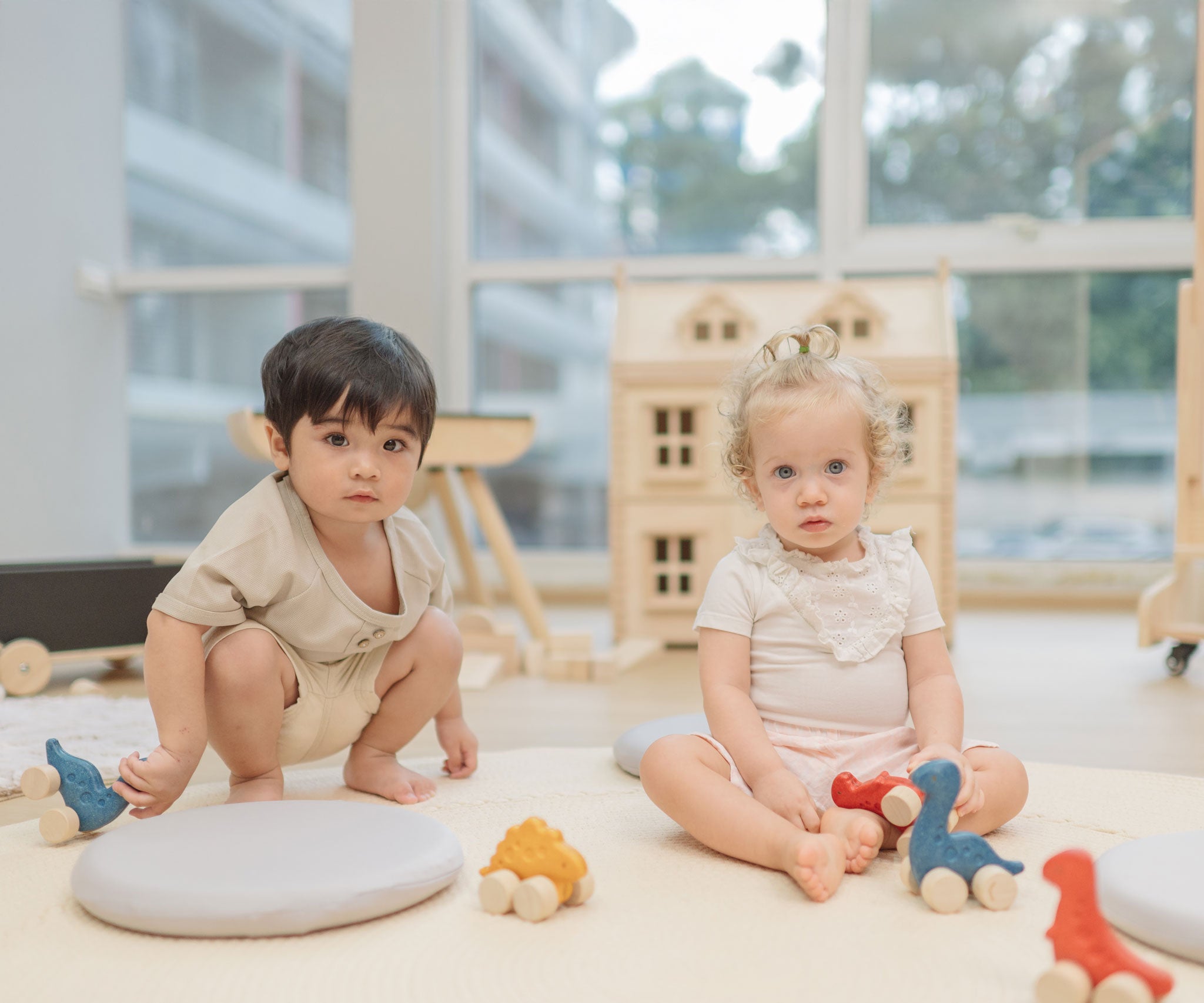 Two children playing with the PlanToys Dino wooden Car toys. A blue coloured diplodocus, a yellow stegosaurus and red coloured t-rex dinosaur figures on wheels. PlanToys range of toys are made from sustainably sourced rubberwood, we're proud stockists of PlanToys here at Babipur. 