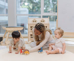 Two children and an adult playing with the PlanToys Dino wooden Car toys. A blue coloured diplodocus, a yellow stegosaurus and red coloured t-rex dinosaur figures on wheels. PlanToys range of toys are made from sustainably sourced rubberwood, we're proud stockists of PlanToys here at Babipur. 