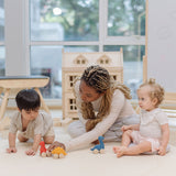 Two children and an adult playing with the PlanToys Dino wooden Car toys. A blue coloured diplodocus, a yellow stegosaurus and red coloured t-rex dinosaur figures on wheels. PlanToys range of toys are made from sustainably sourced rubberwood, we're proud stockists of PlanToys here at Babipur. 