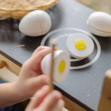 Child holding wooden knife next to a PlanToys egg to cut